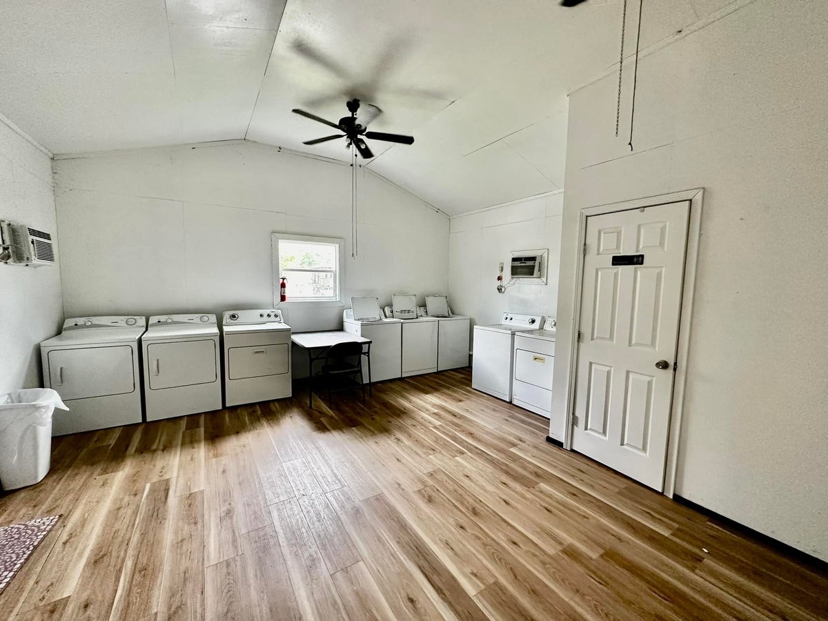 Bright laundry room with wood flooring, multiple washing machines and dryers, white cabinetry, and a ceiling fan at Old River RV Park
