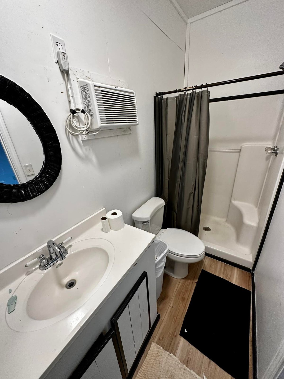Clean shower room with white sink, toilet, shower with gray curtain, and round mirror at Old River RV Park