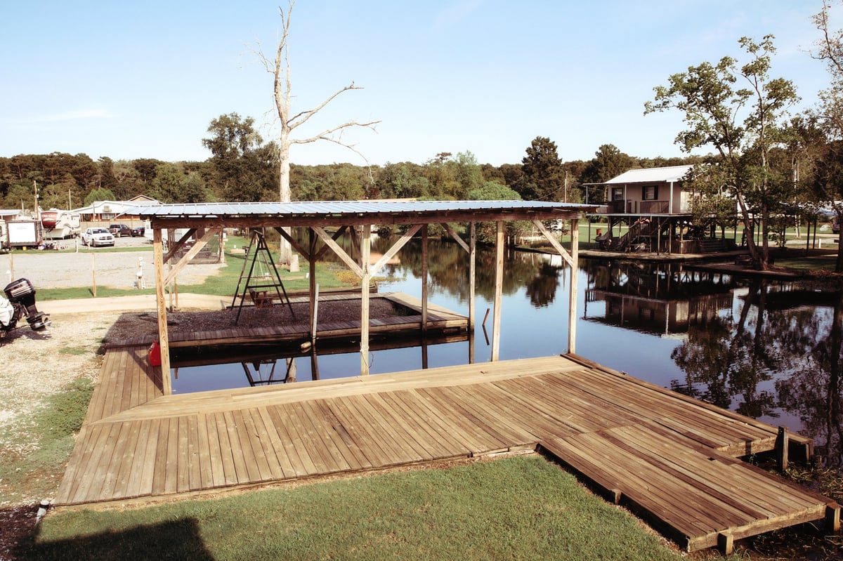Wooden dock and covered boat shelter extending over calm water at Old River RV Park